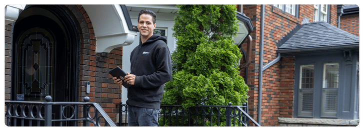 HVAC technician in black hoodie standing at a residential entrance, holding a tablet, showcasing Laird & Son's commitment to quality service in the Greater Toronto Area.