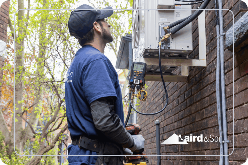 Technician performing maintenance on HVAC system outdoors, featuring Laird & Son branding, surrounded by greenery and brick wall, emphasizing HVAC services and membership plans.